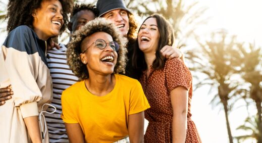 Multi-racial group of friends laughing outdoors with the sun shining through the trees.